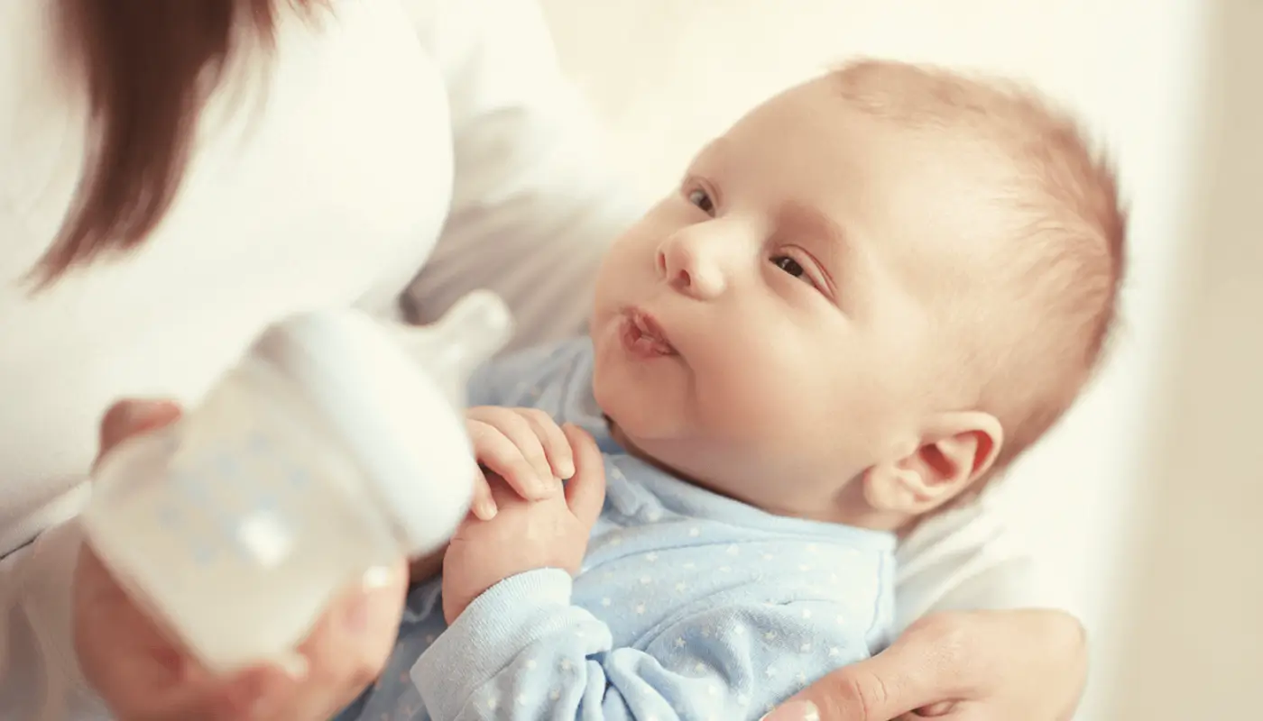 Mãe com mamadeira na mão e com bebê no colo